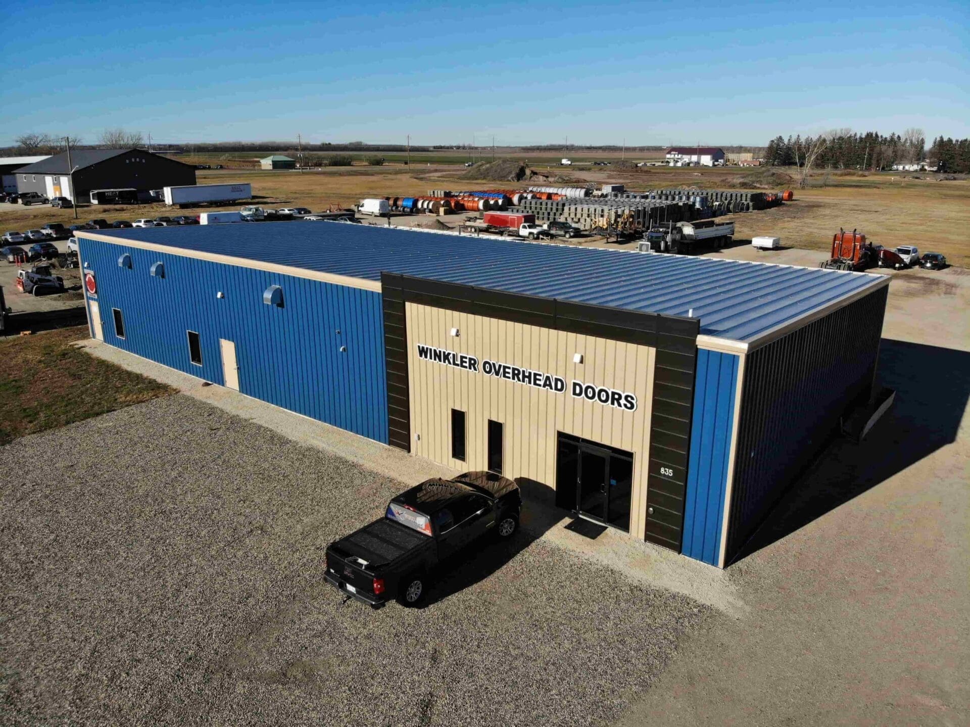 Blue Commercial building with gates and trucks Winkler Overhead Doors and black car